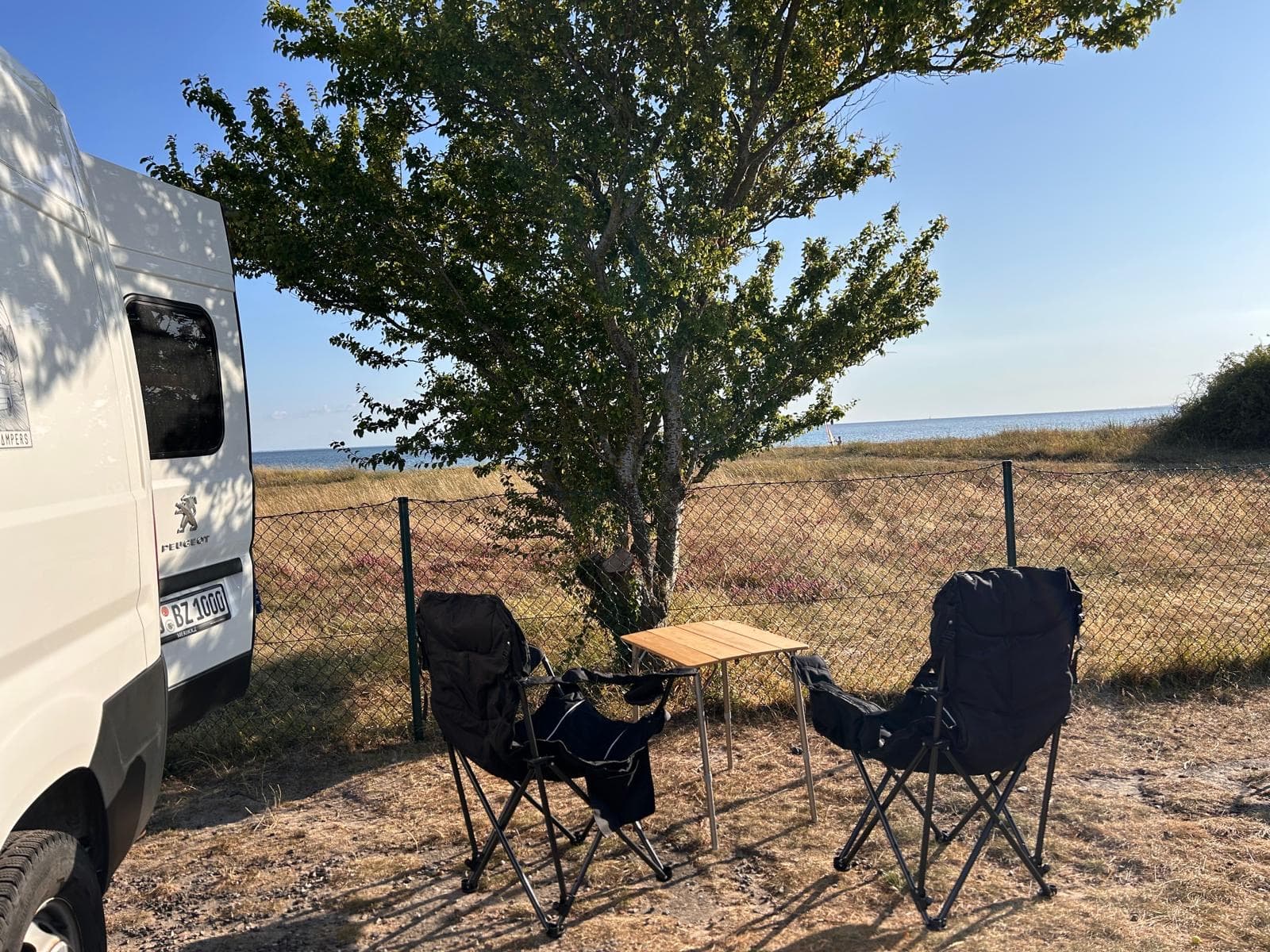 Camper am Strand mit Stühlen unter einem Baum