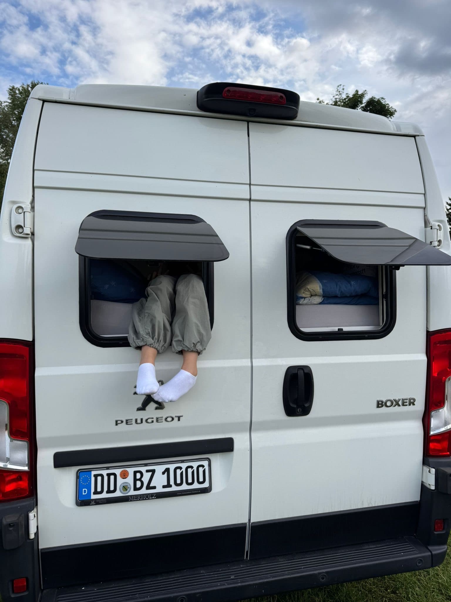Füße in Socken schauen aus dem Heckfenster des Campers